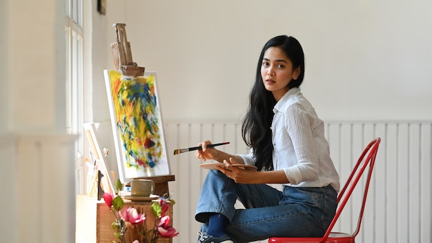 Portrait girl artiste concentré sur la peinture assis devant une toile de dessin sur un atelier moderne et ordonné