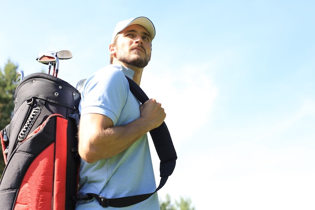 Photo portrait de golfeur masculin portant un sac de golf en marchant par l'herbe verte du club de golf.