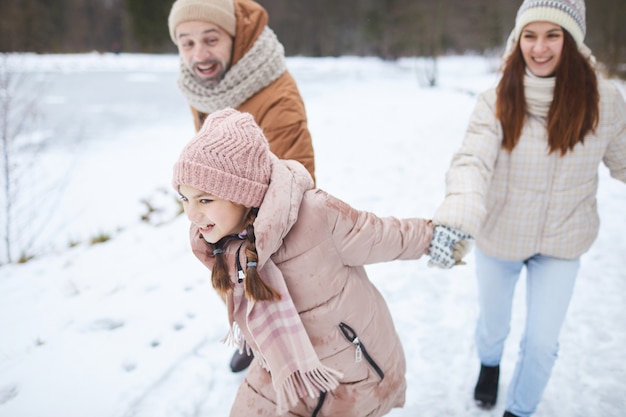 Portrait En Grand Angle D'une Adolescente Enjouée Tenant La Main De Ses Parents Et Les Tirant Tout En Profitant D'une Promenade En Famille Dans La Forêt D'hiver