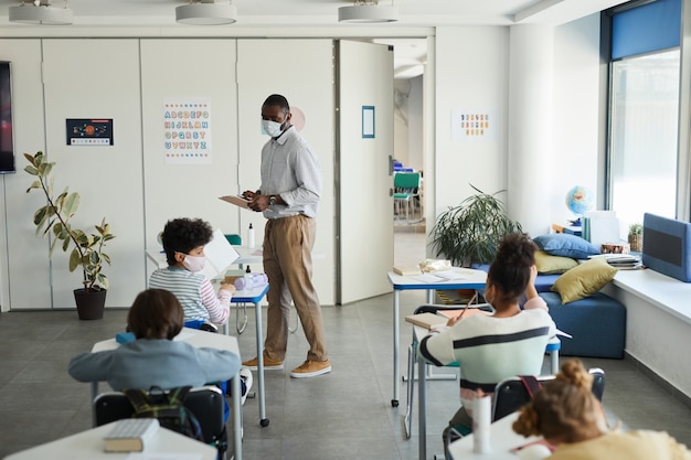 Portrait grand angle d'un enseignant afro-américain portant un masque dans une salle de classe, mesures de sécurité covid, espace de copie