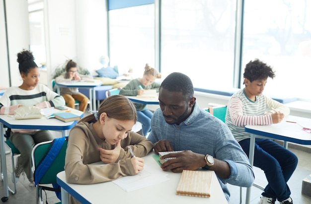 Portrait en grand angle d'un enseignant attentionné aidant une jeune fille dans une salle de classe, espace pour copie