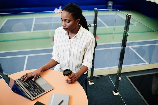 Portrait en grand angle d'une jeune femme noire utilisant un ordinateur portable dans l'espace de copie du centre d'entraînement sportif