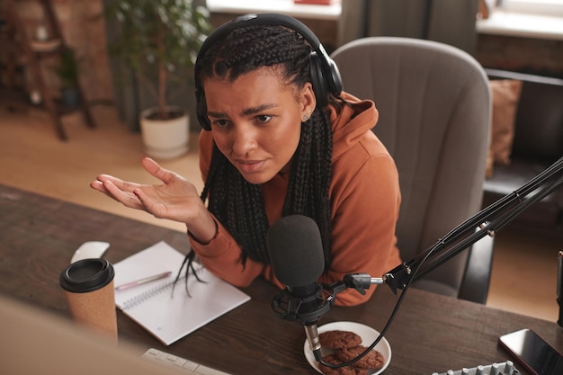 Portrait en grand angle d'une jeune influenceuse portant des écouteurs assis au bureau se sentant confu