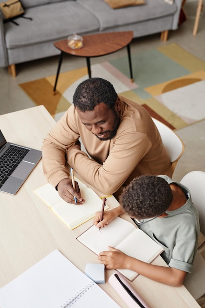 Photo portrait en grand angle d'un père attentionné aidant son fils à faire ses devoirs tout en étudiant à la maison, espace de copie