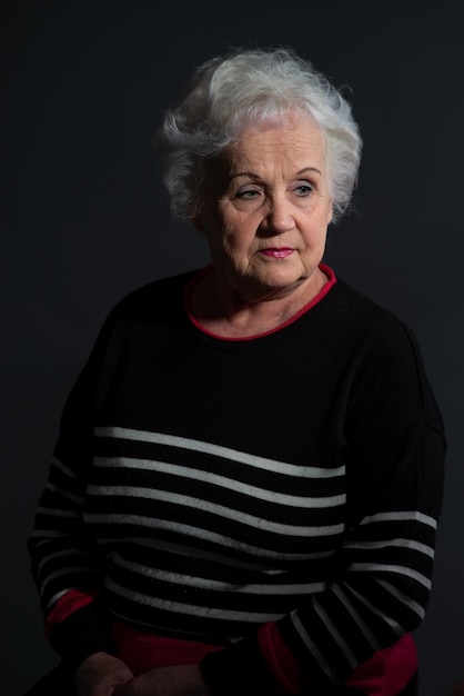 Portrait d'une grand-mère dans un pull sombre sur fond sombre