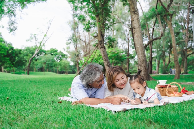 Photo portrait de grands-parents asiatiques et petite-fille portant sur le champ de verre vert en plein air, famille appréciant pique-nique ensemble dans le concept de la journée d'été