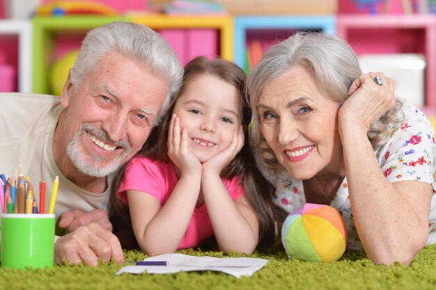 Portrait de grands-parents jouant avec sa petite-fille allongée sur le sol