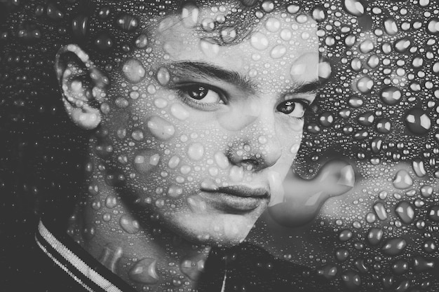Portrait en gros plan d'un adolescent vu à travers un verre mouillé