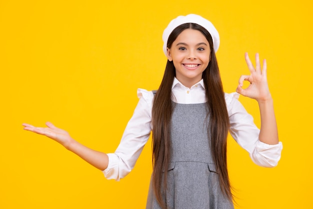 Portrait en gros plan d'une adolescente enfant montrant à l'espace de copie pointant vers des annonces publicitaires isolées sur fond jaune Espace de copie maquette Visage heureux émotions positives et souriantes