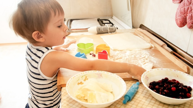 Portrait en gros plan d'un adorable petit garçon de 3 ans préparant des biscuits et de la pâte à rouler avec une broche en bois