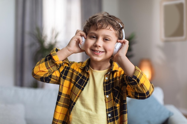 Portrait en gros plan d'un adorable petit garçon heureux appréciant la musique via des écouteurs sans fil souriant à la caméra posant à la maison