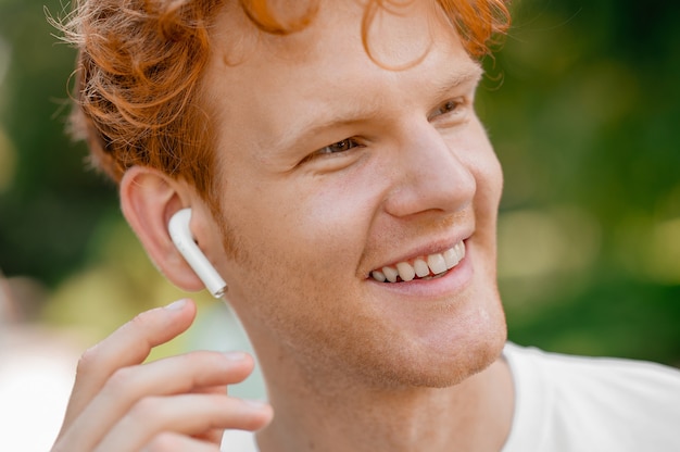 Portrait en gros plan d'un beau mec souriant aux cheveux roux courts portant les écouteurs intra-auriculaires