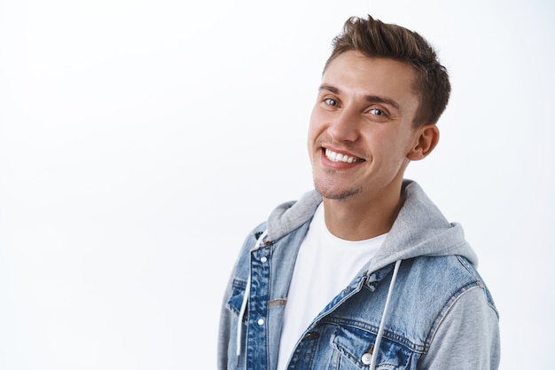 Portrait en gros plan d'un bel homme blond gai avec des poils, rayonnant de sourire heureux, regardant la caméra ravie, exprimant la joie, la bonne humeur et la positivité, mur blanc debout