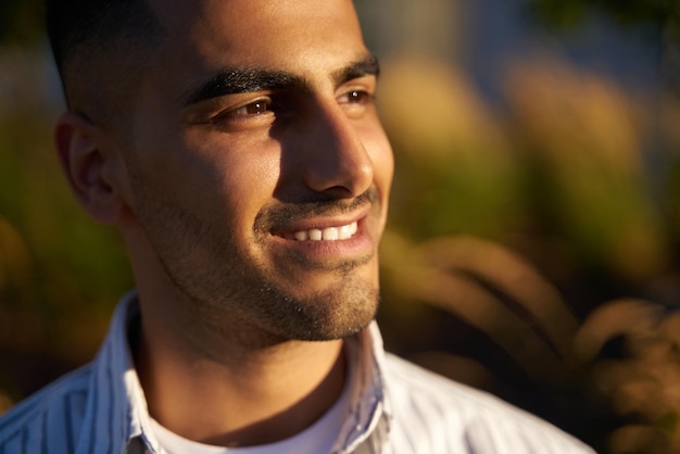 Portrait en gros plan d'un bel homme souriant du Moyen-Orient regardant loin en profitant du coucher du soleil dans le parc