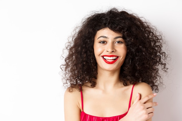 Portrait de gros plan de la belle dame aux cheveux bouclés et aux lèvres rouges, souriant et riant heureux, debout sur fond blanc.