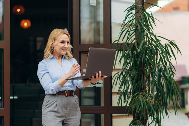 Portrait en gros plan d'une belle femme d'affaires de 50 ans Utilisez votre ordinateur portable à l'extérieur près du bureau