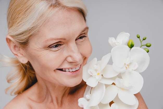 Portrait en gros plan d'une belle femme d'âge moyen avec une branche d'orchidée isolée sur un fond gris