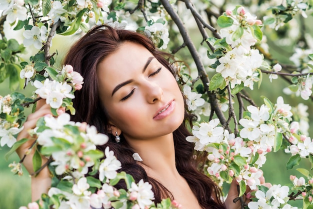 Portrait en gros plan d'une belle femme dans un jardin de printemps. Une fille aux yeux fermés inhale le parfum des arbres en fleurs.