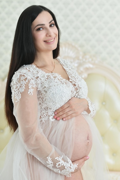 Portrait en gros plan d'une belle femme enceinte posant à la maison avec des vêtements de bébé