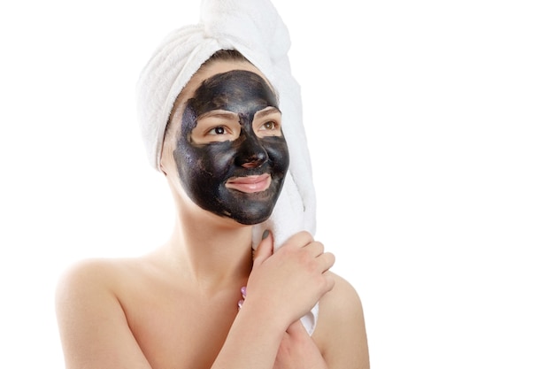 Portrait en gros plan belle femme avec masque facial noir sur fond blanc, fille avec une serviette blanche sur la tête, sourire satisfait et heureux