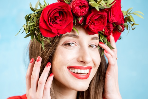 Portrait en gros plan d'une belle femme en robe rouge avec une couronne de roses rouges sur fond bleu