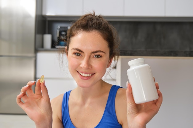 Portrait en gros plan d'une belle femme souriante de remise en forme montrant une bouteille de vitamine avec un complément alimentaire