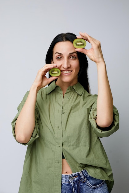 Portrait en gros plan d'une belle femme souriante et tenant des kiwis devant ses yeux