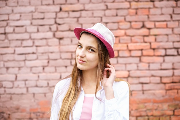 Photo portrait en gros plan d'une belle fille élégante en chapeau près d'un mur de briques roses en arrière-plan