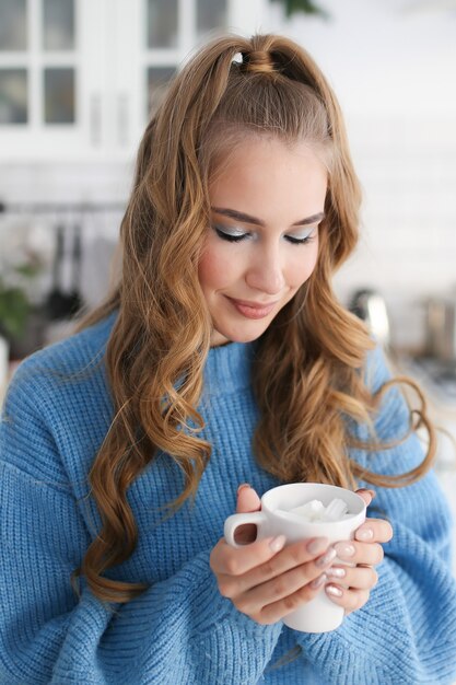 Portrait en gros plan d'une belle fille mignonne heureuse avec une coiffure dans un pull bleu dans une cuisine