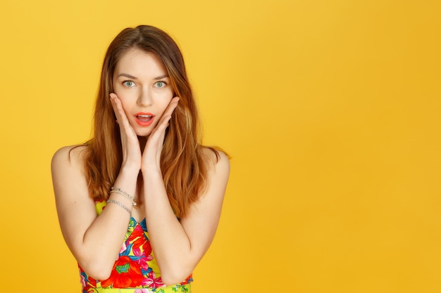 Portrait de gros plan d'une belle fille surprise, tenant sa tête avec étonnement et bouche bée. Sur fond blanc.