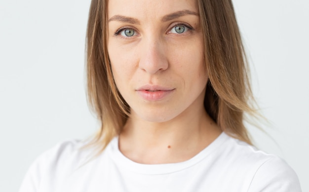 Portrait en gros plan d'une belle jeune femme caucasienne regardant sur le côté posant sur fond de mur blanc. Le concept d'une belle femme soignée. Espace de copie