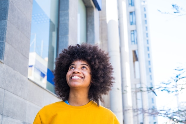 Portrait en gros plan d'une belle jeune femme noire souriante à l'extérieur dans la rue d'une ville grise - femme d'affaires marchant et s'amusant seule