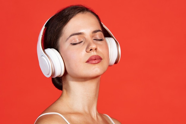 Portrait en gros plan d'une belle jeune femme posant dans un casque blanc isolé sur un studio rouge