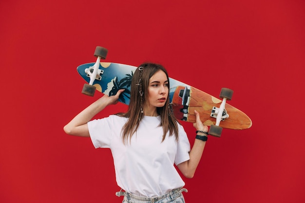 Portrait en gros plan d'une belle jeune femme skateuse tenant sa longue planche colorée