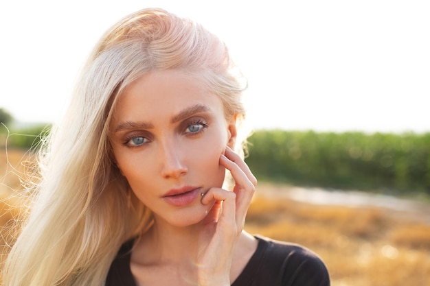 Portrait en gros plan d'une belle jeune fille blonde aux yeux bleus sur fond de lumière du soleil Photo naturelle en plein air