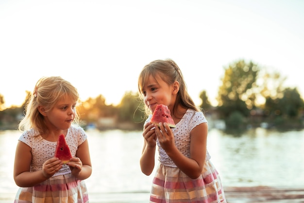 Portrait en gros plan d'une belle jeune fille mangeant une tranche de pastèque au coucher du soleil au bord de l'étang