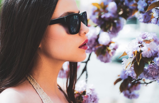 Portrait en gros plan d'une belle jeune fille à la peau propre sur un joli visage sur fond de fleur de printemps