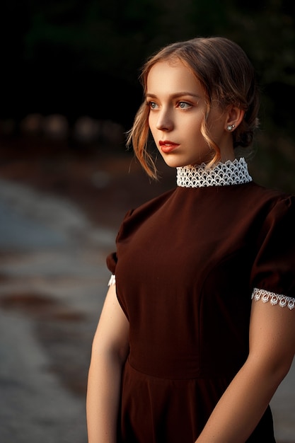 Portrait en gros plan d'une belle jeune fille vêtue d'une robe marron dans un style rétro sur une route abandonnée.