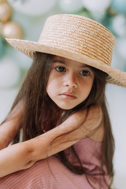 Portrait en gros plan d'une belle petite fille aux yeux bruns et aux cheveux noirs en chapeau de paille