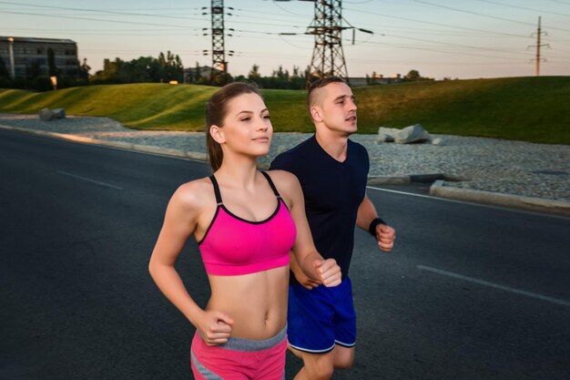 Portrait en gros plan d'un couple athlétique courant sur la route, de jeunes coureurs musclés s'entraînant en faisant du jogging dans le parc. Soir