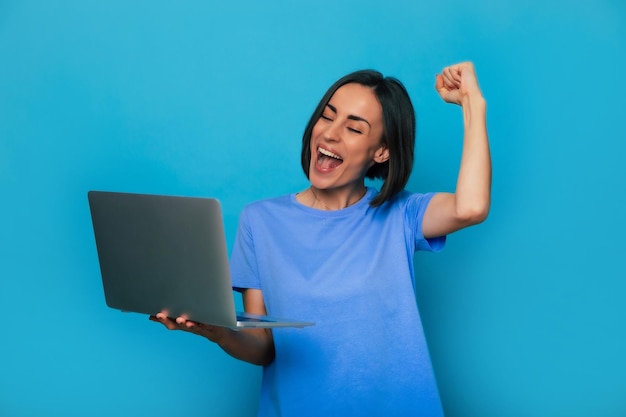 Portrait en gros plan de cris et d'une belle femme moderne excitée alors qu'elle tient un ordinateur portable et célèbre sa victoire dans un pari ou une loterie et lève le poing