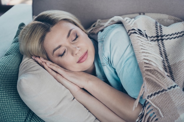 Portrait de gros plan de dame allongée sur un divan recouvert de sommeil de voile à carreaux