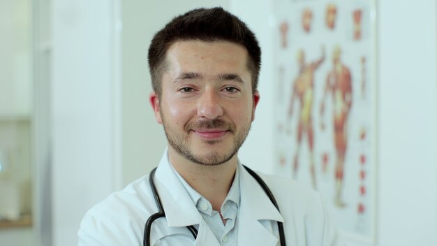 Portrait en gros plan du médecin de famille est dans une clinique de santé. Un médecin réussi en blouse blanche regarde la caméra dans le bureau de l'hôpital.