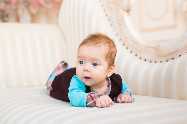 Portrait en gros plan du petit garçon aux cheveux roux et aux yeux bleus. Nouveau-né couché dans le canapé.