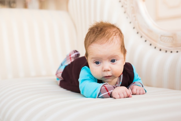 Portrait en gros plan du petit garçon aux cheveux roux et aux yeux bleus. Nouveau-né couché dans le canapé.