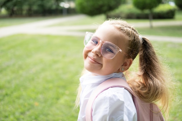 portrait en gros plan d'une écolière blonde à lunettes chemise blanche avec sac à dos rose retour à l'école