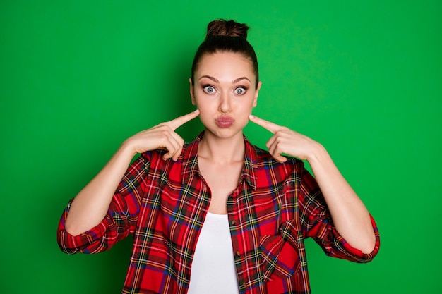 Portrait en gros plan d'elle, elle, jolie, jolie et jolie fille drôle de jeune fille soufflant des joues pointant des index isolés sur un fond de couleur vert vif et brillant