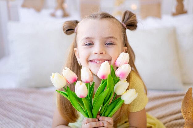 Portrait en gros plan d'un enfant mignon avec des fleurs de printemps tulipes roses souriant et se réjouissant ou offrant en cadeau la fête des femmes ou la fête des mères