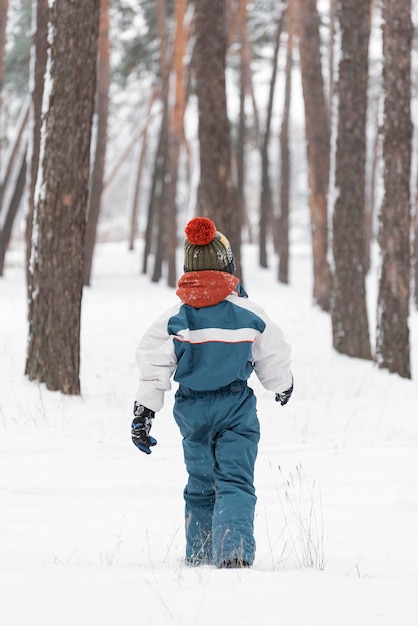 Portrait en gros plan d'un enfant en vêtements d'hiver. Le garçon longe la forêt enneigée. Vue arrière