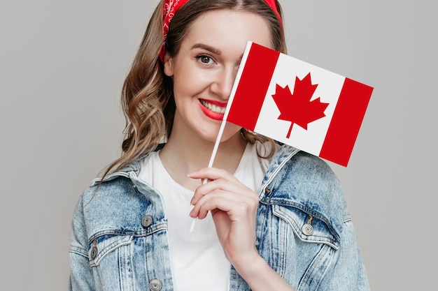 Portrait en gros plan d'une étudiante souriante et tenant un petit drapeau du canada isolé sur fond gris, fête du Canada, vacances, anniversaire de la confédération, espace de copie